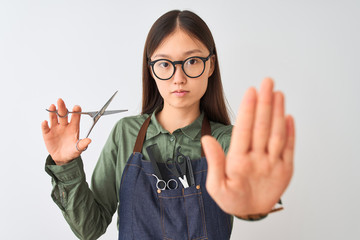 Chinese hairdresser woman wearing glasses holding scissors over isolated white background with open hand doing stop sign with serious and confident expression, defense gesture