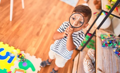 Obraz na płótnie Canvas Beautiful toddler boy using magnifying glass at kindergarten