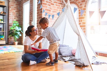 Beautiful teacher and toddler boy sitting on the floor playing inside  tipi at kindergarten