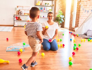 Beautiful teacher and toddler boy playing with colored small balls at kindergarten
