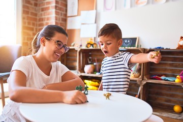Beautiful teacher and toddler boy playing with figurine army soldiers at kindergarten