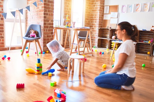 Beautiful teacher and toddler boy playing with plastic basket at kindergarten