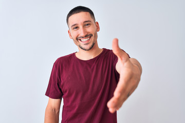 Young handsome man standing over isolated background smiling friendly offering handshake as greeting and welcoming. Successful business.