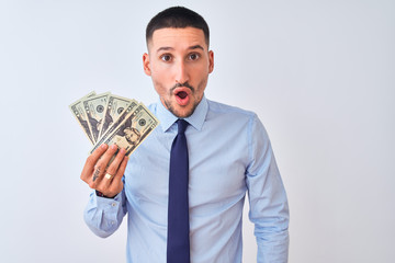Young handsome business man holding a bunch of bank notes dollars over isolated background scared in shock with a surprise face, afraid and excited with fear expression