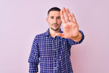 Young handsome man standing over isolated background doing stop sing with palm of the hand. Warning...