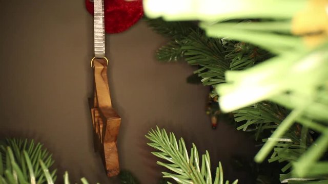 Puling away from a sideways wooden star Christmas ornament, back through branches of an artificial Christmas tree, next to a white ornament with silver top and a red ribbon.