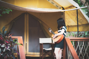happy young cute female Asian woman Japanese girl women hipster play guitar at tent camping campfire  party at beautiful blue sky scenery river lake waterfall green forest Kanchanaburi, Thailand