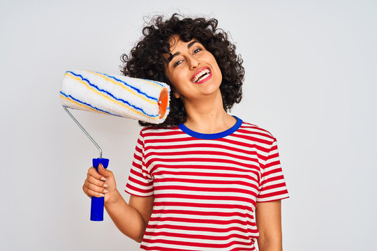 Young arab painter woman with curly hair holding paint roller over isolated white background with a happy face standing and smiling with a confident smile showing teeth