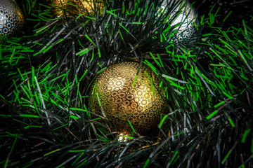 Beautiful shiny golden bauble among green tinsel - closeup