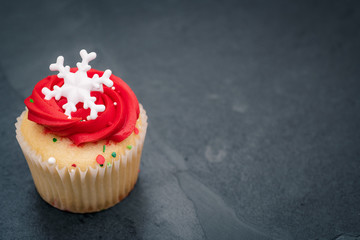 White cupcake with red frosting and sprinkles with a white snowflake on a slate background