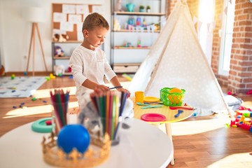 Beautiful blonde toddler playing with plastic food and dishes. Standing around lots of toys at kindergarten