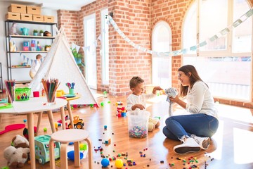 Beautiful teacher and toddlers playing around lots of toys at kindergarten