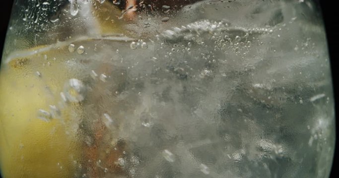 Macro of a professional bartender is mixing a gin tonic with professional crystal ice cubes to customers at the bar or disco club.