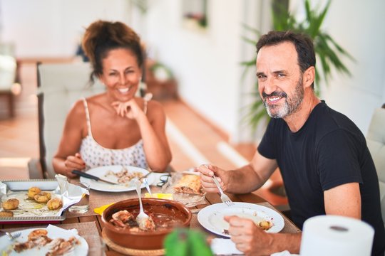 Middle age beautiful couple sitting on terrace eating food speaking and smiling