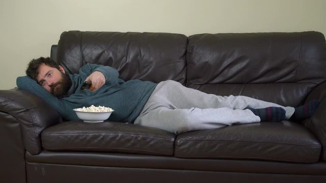 Man Changing Channels with Remote Control, Watching Television on Sofa