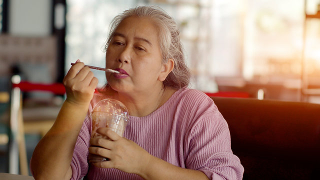 Asian senior woman drinking ice chocolate happily in coffee shop - Powered by Adobe