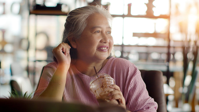 Asian senior woman drinking ice chocolate happily in coffee shop