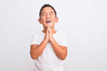 Beautiful kid boy wearing casual t-shirt standing over isolated white background begging and praying with hands together with hope expression on face very emotional and worried. Asking