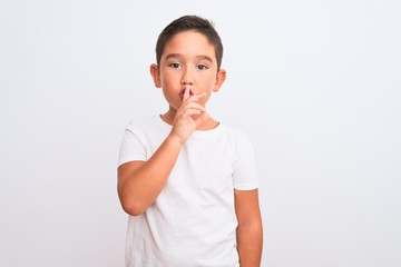 Beautiful kid boy wearing casual t-shirt standing over isolated white background asking to be quiet with finger on lips. Silence and secret concept.