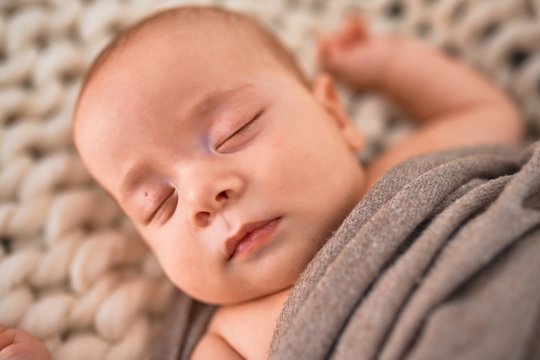 Adorable baby lying down on the sofa over blanket at home. Newborn relaxing and sleeping comfortable