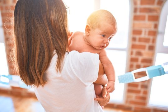 Young beautifull woman and her baby standing at home. Mother holding and hugging newborn