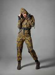 Portrait of a serious angry grumpy young female keeping arms folded. Dressed in raincoat posing with hood on her head and looking at camera isolated over gray background.