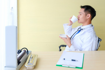 Young male Asian doctor is drinking coffee  in the office at the hospital.medical technology, disease treatment and health care concept