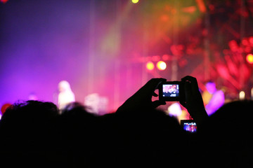 Silhouettes of people at music concert taking photos with camera.