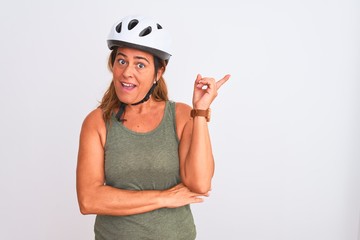 Middle age mature cyclist woman wearing safety helmet over isolated background with a big smile on face, pointing with hand finger to the side looking at the camera.