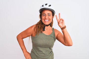 Middle age mature cyclist woman wearing safety helmet over isolated background smiling looking to the camera showing fingers doing victory sign. Number two.