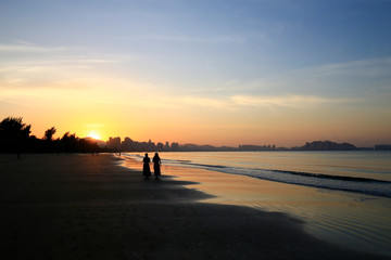 Two women by the sea, silhouetted by the sunrise