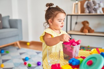 Beautiful toddler playing with building wooden blocks toys at kindergarten