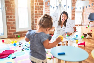 Beautiful psycologist and toddler girl sitting on the floor doing therapy using emoji emotions at consulting room