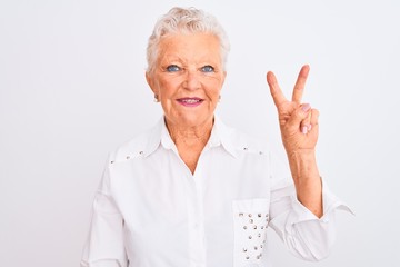 Senior grey-haired woman wearing elegant shirt standing over isolated white background smiling with happy face winking at the camera doing victory sign. Number two.