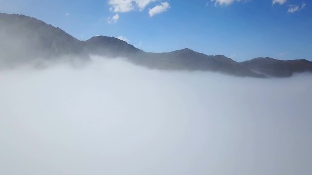 Peak of foggy green mountains and cloudscape under blue sky