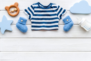 Newborn baby boy set - blue clothes as bodysuit, booties, toys - on white wooden table top-down...