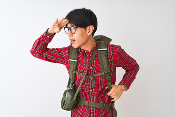 Chinese hiker man wearing backpack canteen glasses over isolated white background very happy and smiling looking far away with hand over head. Searching concept.
