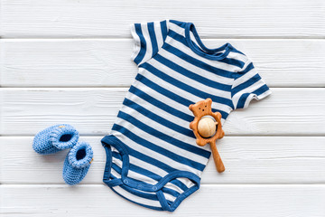 Blue bodysuit for baby boy near children's accessories on white wooden background top-down copy space