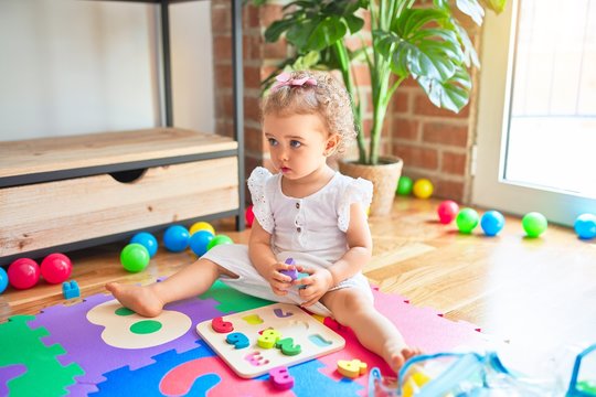 Beautiful caucasian infant playing with toys at colorful playroom. Happy and playful at kindergarten.