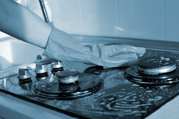 A hand In a rubber glove cleans a gas stove. Kitchen cleaning. Blue color toned