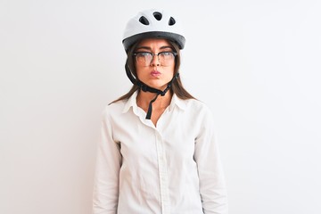 Beautiful businesswoman wearing glasses and bike helmet over isolated white background puffing cheeks with funny face. Mouth inflated with air, crazy expression.
