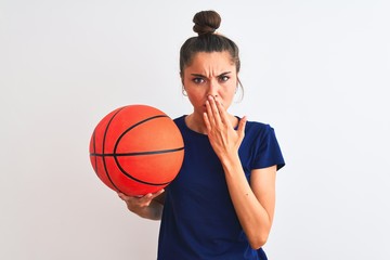 Young beautiful sportswoman holding basketball ball over isolated white background cover mouth with hand shocked with shame for mistake, expression of fear, scared in silence, secret concept