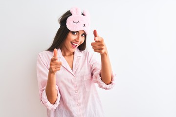 Young beautiful woman wearing sleep mask and pajama over isolated white background pointing fingers to camera with happy and funny face. Good energy and vibes.