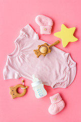 Pink bodysuit for baby girl near children's things on pink background top-down