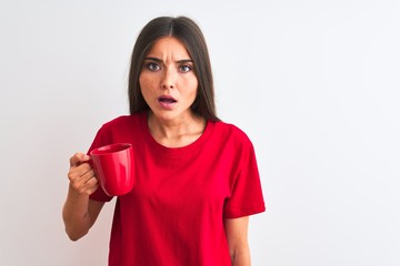 Young beautiful woman drinking red cup of coffee standing over isolated white background scared in shock with a surprise face, afraid and excited with fear expression