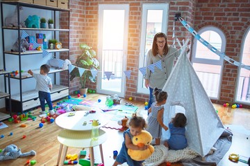 Beautiful teacher and group of toddlers playing around lots of toys at kindergarten