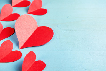 Red hearts cut out of paper on a blue background. Copy space