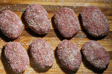 burgers for frying in breadcrumbs on a wooden tray