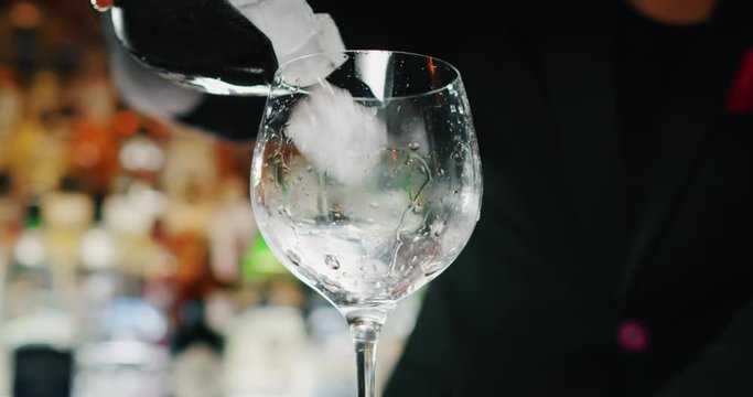 Close up of a professional bartender is putting professional crystal long lasting ice cubes for preparation an alcoholic cocktail with to customers at the bar or disco club.