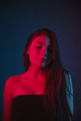 Slim, beautiful young girl in black top posing in neon red and blue light